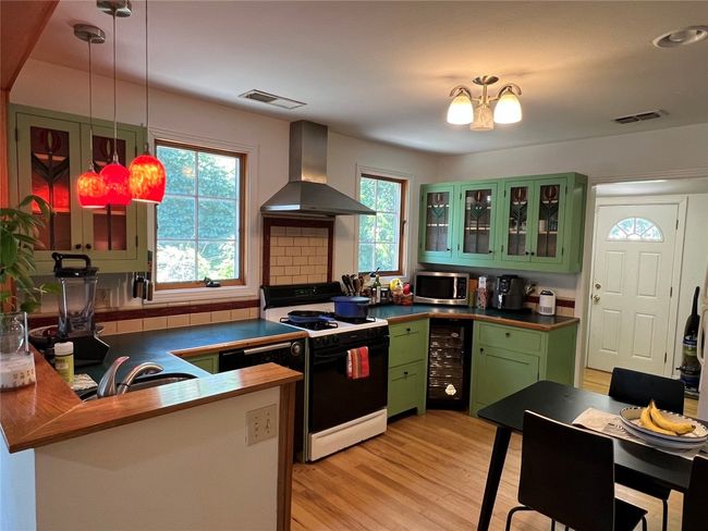 Kitchen with stainless steel microwave, range with gas stovetop, wall chimney range hood, visible vents, and green cabinetry | Image 4
