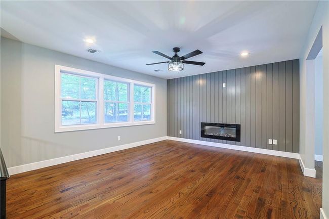 Unfurnished living room featuring hardwood / wood-style flooring, a large fireplace, and ceiling fan | Image 6