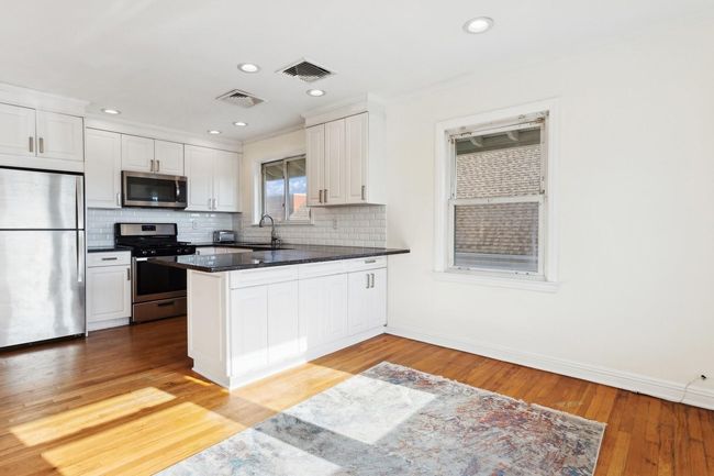 Kitchen featuring a peninsula, visible vents, white cabinets, and stainless steel appliances | Image 7