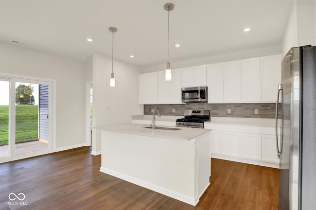 kitchen with stainless steel appliances, a sink, backsplash, dark wood-type flooring, and light countertops | Image 5