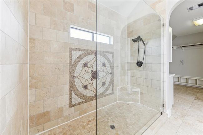 This elegant bathroom features a spacious walk-in shower with a glass enclosure, decorative tile accent, and a modern shower head. The neutral tile design and built-in bench add functionality and style. | Image 18
