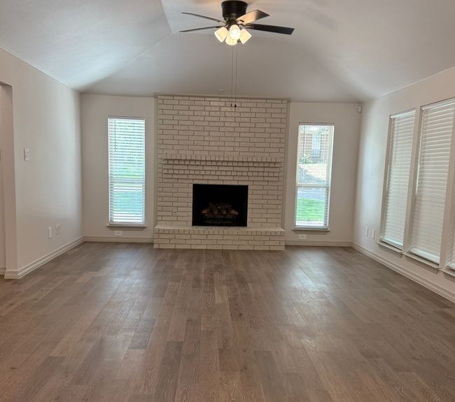 Living room with lofted ceiling, ceiling fan, wood finished floors, and a fireplace | Image 4