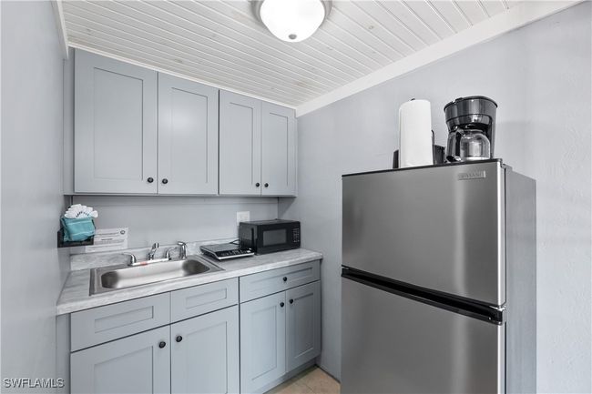Kitchen with gray cabinets, stainless steel refrigerator, ornamental molding, wooden ceiling, and sink | Image 22