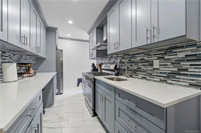 Kitchen featuring appliances with stainless steel finishes, decorative backsplash, wall chimney range hood, and gray cabinetry | Image 2