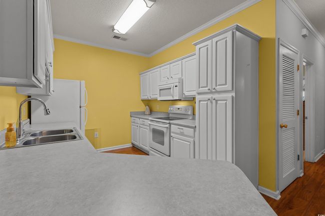 Kitchen with white appliances, a sink, crown molding, dark wood-type flooring, and baseboards | Image 13
