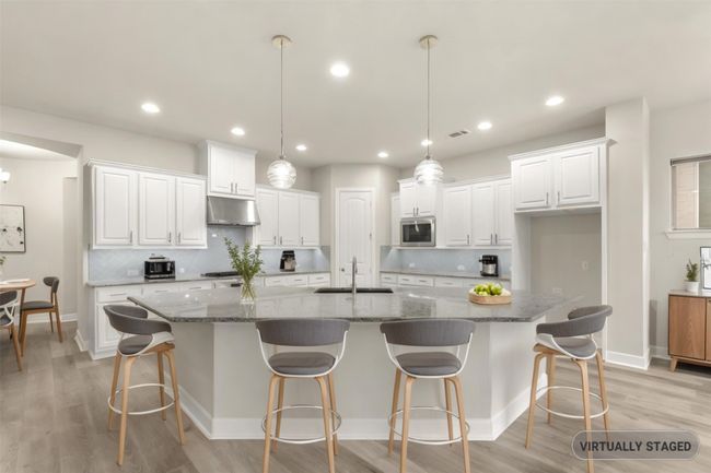 Virtually staged Kitchen featuring stainless steel microwave, under cabinet range hood, white cabinetry, a sink, and recessed lighting | Image 6