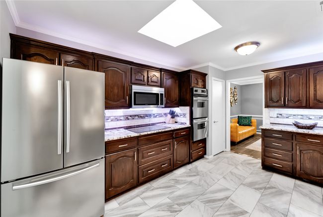 Kitchen featuring appliances with stainless steel finishes, dark brown cabinetry, a skylight, ornamental molding, and decorative backsplash | Image 12