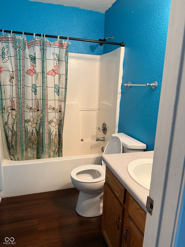 bathroom featuring a textured wall, wood finished floors, shower / bath combo with shower curtain, and vanity | Image 12