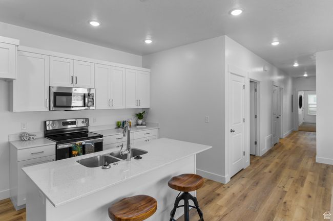 Kitchen with a sink, a breakfast bar, light wood-style flooring, baseboards, and appliances with stainless steel finishes | Image 7