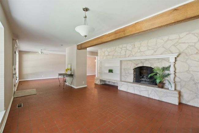 Unfurnished living room with a stone fireplace, a ceiling fan, and brick flooring | Image 8