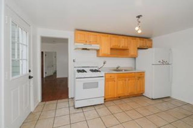 Kitchen with white appliances, under cabinet range hood, light countertops, light tile patterned flooring, and plenty of natural light | Image 30