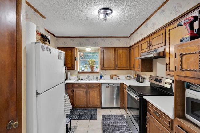 Kitchen featuring stainless steel appliances, under cabinet range hood, a sink, a textured ceiling, and brown cabinetry | Image 9