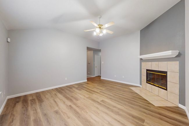 Unfurnished living room featuring a tile fireplace, vaulted ceiling, ceiling fan, light wood finished floors, and baseboards | Image 20