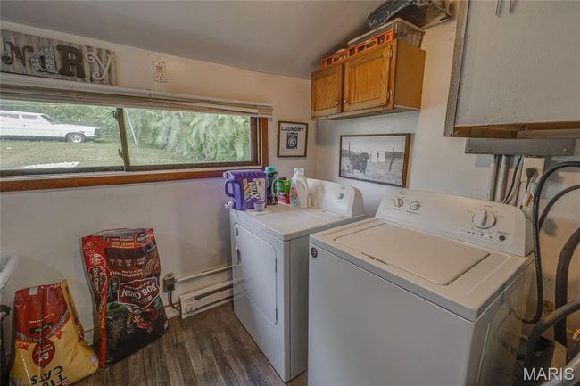 Laundry room featuring washer and dryer, baseboard heating, cabinet space, and dark wood-style flooring | Image 13
