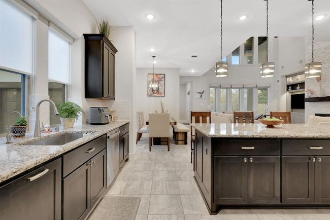This modern kitchen and dining area features sleek granite countertops, dark cabinetry, and stainless steel appliances. It opens to a bright living space with large windows and contemporary lighting, creating an inviting atmosphere ideal for entertaining. | Image 17