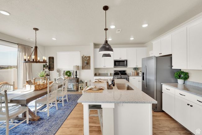 Kitchen with stainless steel appliances, a sink, light wood finished floors, an island with sink, and white cabinets | Image 9