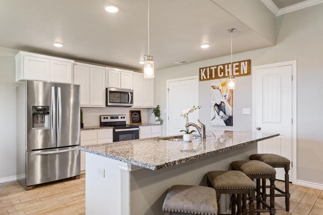 Kitchen featuring appliances with stainless steel finishes, light wood-style floors, white cabinetry, a breakfast bar, and light stone counters | Image 13