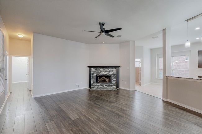 Unfurnished living room with a ceiling fan, dark wood-style floors, a tile fireplace, and baseboards | Image 9