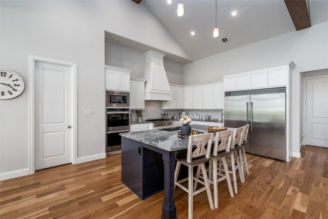 Kitchen featuring built in appliances, high vaulted ceiling, custom exhaust hood, dark stone counters, and tasteful backsplash | Image 11