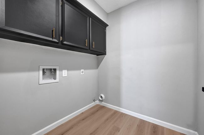 This dedicated utility room offers upper cabinetry with bold black finishes and gold hardware, providing stylish storage space for laundry essentials. The room is equipped with full washer and dryer connections and updated flooring for a clean, modern look. | Image 34