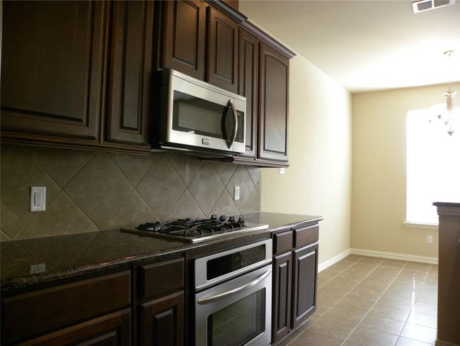 Kitchen with stainless steel appliances, dark brown cabinets, backsplash, and dark stone counters | Image 8