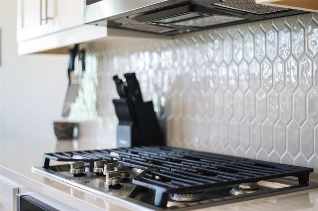 Kitchen view of stainless steel gas stovetop, white cabinets, decorative backsplash, and extractor fan | Image 12