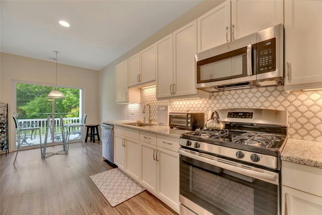 Kitchen featuring stainless steel appliances, backsplash, wood finished floors, white cabinetry, and pendant lighting | Image 9
