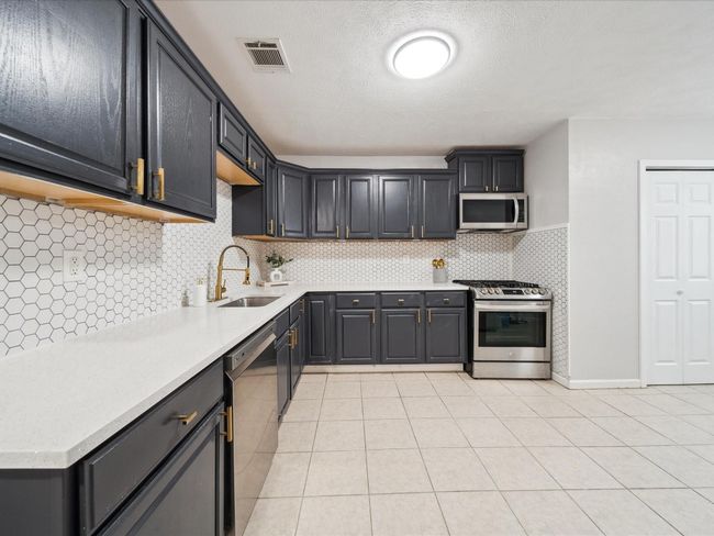 Kitchen with stainless steel appliances, a sink, light countertops, light tile patterned floors, and a textured ceiling | Image 7