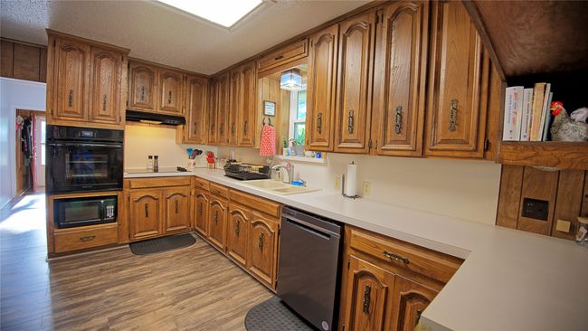 Kitchen with brown cabinets, light wood finished floors, under cabinet range hood, light countertops, and black appliances | Image 5