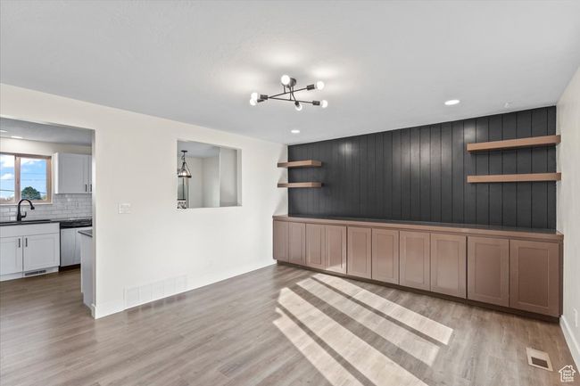 Unfurnished living room with light wood finished floors, visible vents, a sink, and an inviting chandelier | Image 5