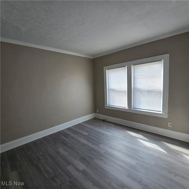 Empty room featuring dark wood-type flooring, a textured ceiling, crown molding, and baseboards | Image 6