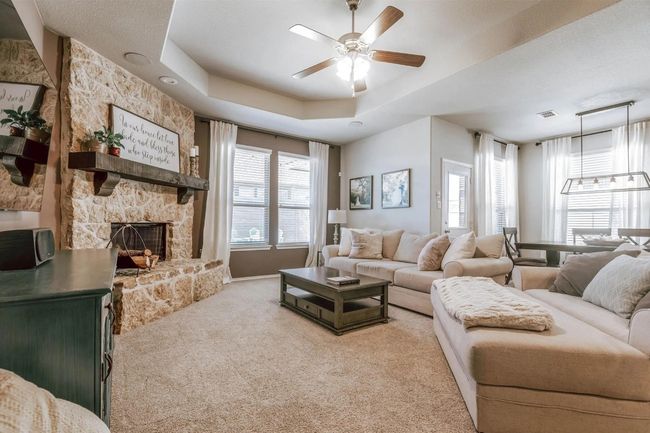 Living area featuring a tray ceiling, light colored carpet, a ceiling fan, and a stone fireplace | Image 18