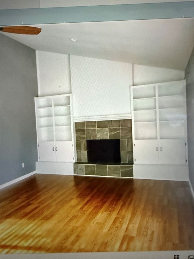 Unfurnished living room with vaulted ceiling, wood finished floors, a tile fireplace, and built in shelves | Image 7