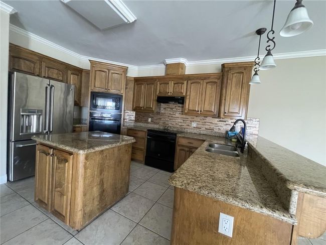 Kitchen featuring black appliances, crown molding, under cabinet range hood, light stone counters, and decorative backsplash | Image 10