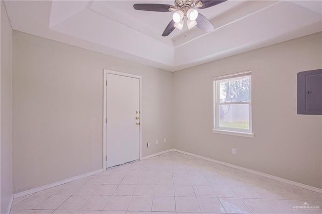Empty room featuring ceiling fan, electric panel, baseboards, light tile patterned flooring, and a tray ceiling | Image 25