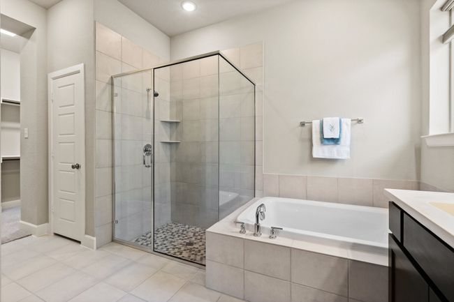 Beautiful tiled primary bathroom with separate tub and shower, separate commode room, linen closet, and double vanity. | Image 30
