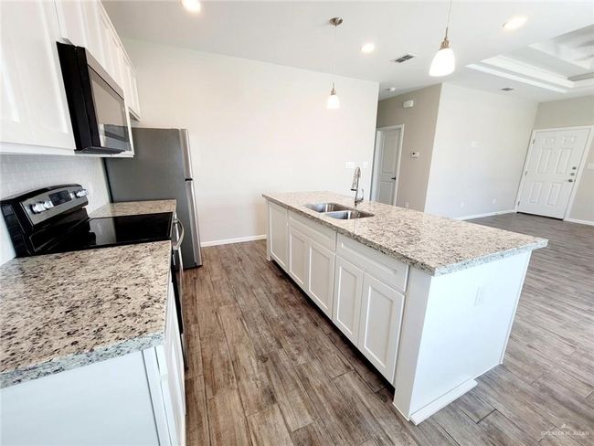 Kitchen featuring a sink, stainless steel appliances, white cabinetry, wood finished floors, and recessed lighting | Image 14