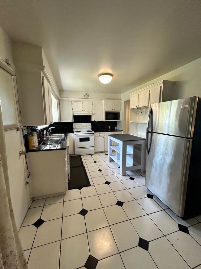 Kitchen with dark countertops, black microwave, a sink, freestanding refrigerator, and white electric range | Image 15