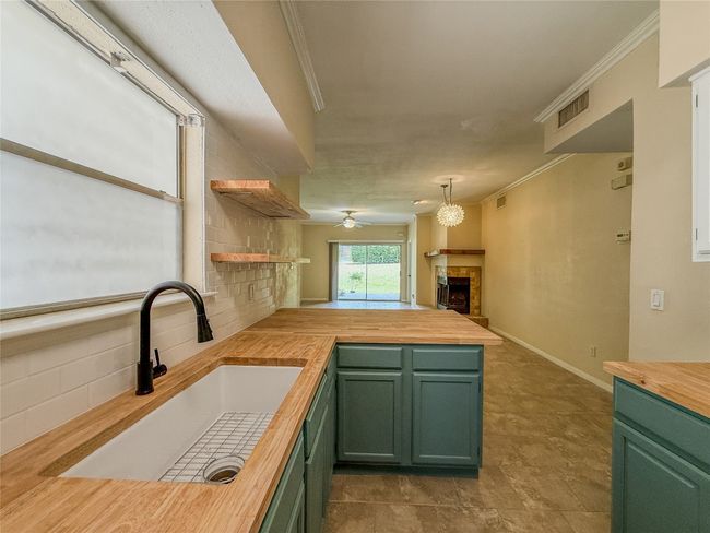 Kitchen with wood counters, green cabinetry, a peninsula, ornamental molding, and a tile fireplace | Image 16