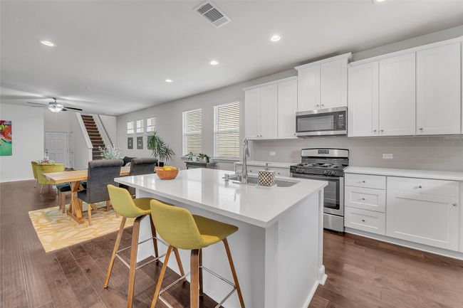 Kitchen featuring appliances with stainless steel finishes, a sink, dark wood-type flooring, a center island with sink, and light countertops | Image 5