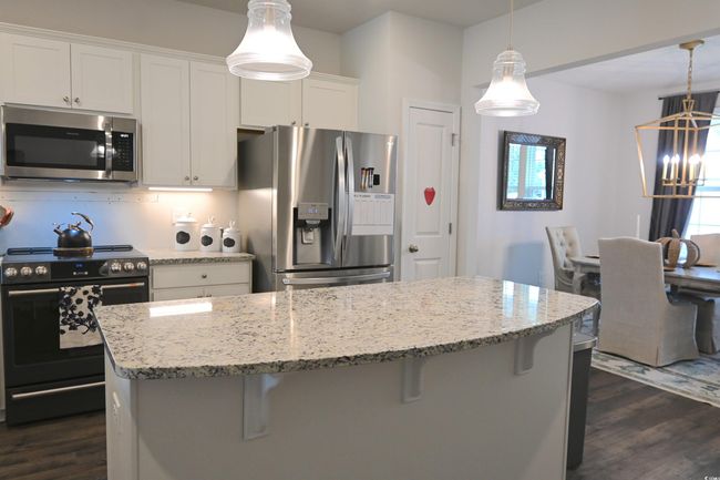 Kitchen featuring stainless steel appliances, dark wood-style flooring, a kitchen breakfast bar, and light stone countertops | Image 8