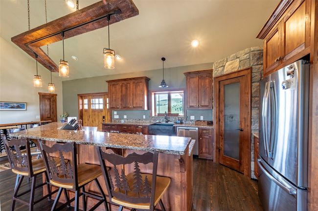Kitchen featuring appliances with stainless steel finishes, dark wood-type flooring, a center island, a sink, and hanging light fixtures | Image 12