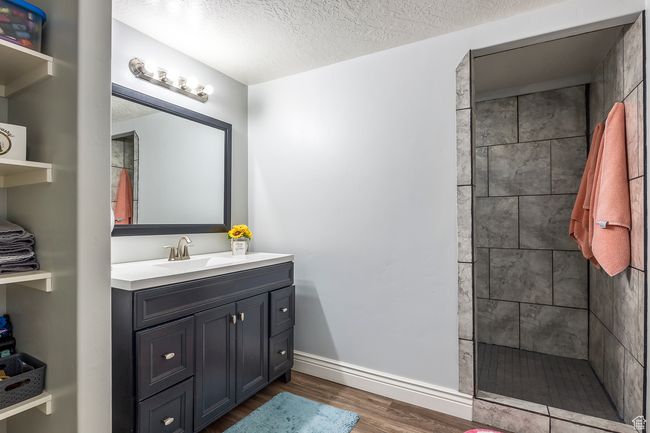 Bathroom with wood-type flooring, a tile shower, vanity, and a textured ceiling | Image 34