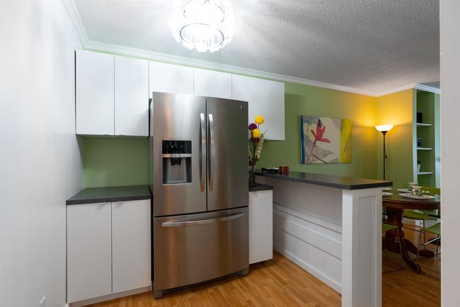 Kitchen with white cabinetry, ornamental molding, dark countertops, a textured ceiling, and stainless steel fridge with ice dispenser | Image 9