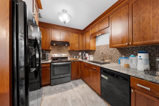Kitchen featuring black appliances, under cabinet range hood, a sink, brown cabinetry, and light wood-type flooring | Image 6