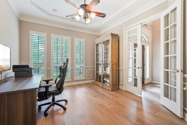 This room features hardwood floors, large windows with shutters for natural light, and French doors. It includes built-in shelving, and a workspace, perfect for a home office. | Image 5