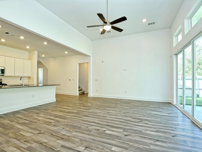Unfurnished living room with light wood finished floors, stairway, ceiling fan, recessed lighting, and a high ceiling | Image 7