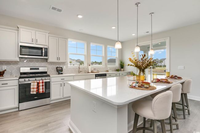 Kitchen featuring appliances with stainless steel finishes, light wood-type flooring, decorative backsplash, a kitchen island, and light countertops | Image 5