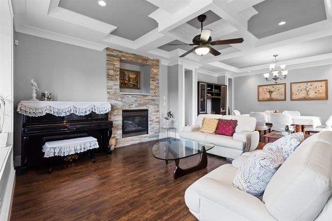 Living room with coffered ceiling, ceiling fan, a fireplace, wood finished floors, and a chandelier | Image 5