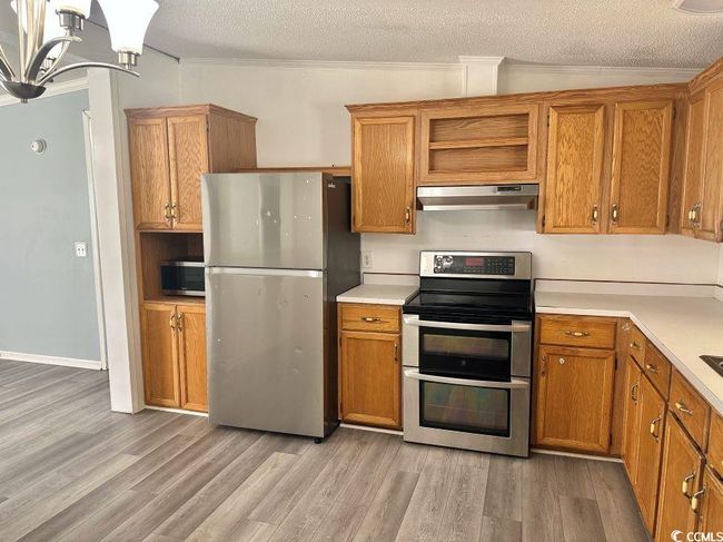 Kitchen with stainless steel appliances, exhaust hood, light wood-type flooring, a textured ceiling, and brown cabinets | Image 7